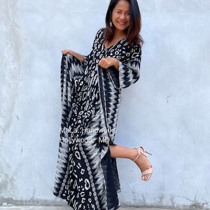 May include: A woman wearing a black and white maxi dress with a geometric pattern. The dress has a V-neckline and long sleeves. She is wearing nude heels and smiling. The text "MaLa Handworks Hollywood MD" is visible on the dress.