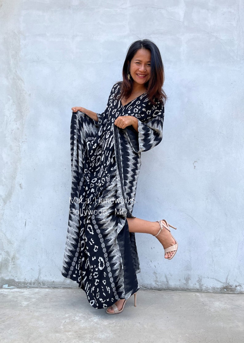 May include: A woman wearing a black and white maxi dress with a geometric pattern. The dress has a V-neckline and long sleeves. She is wearing nude heels and smiling. The text "MaLa Handworks Hollywood MD" is visible on the dress.