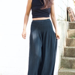 May include: A woman wearing a black crop top and wide-legged black pants. The pants have a smocked waistband and are made of a lightweight fabric.