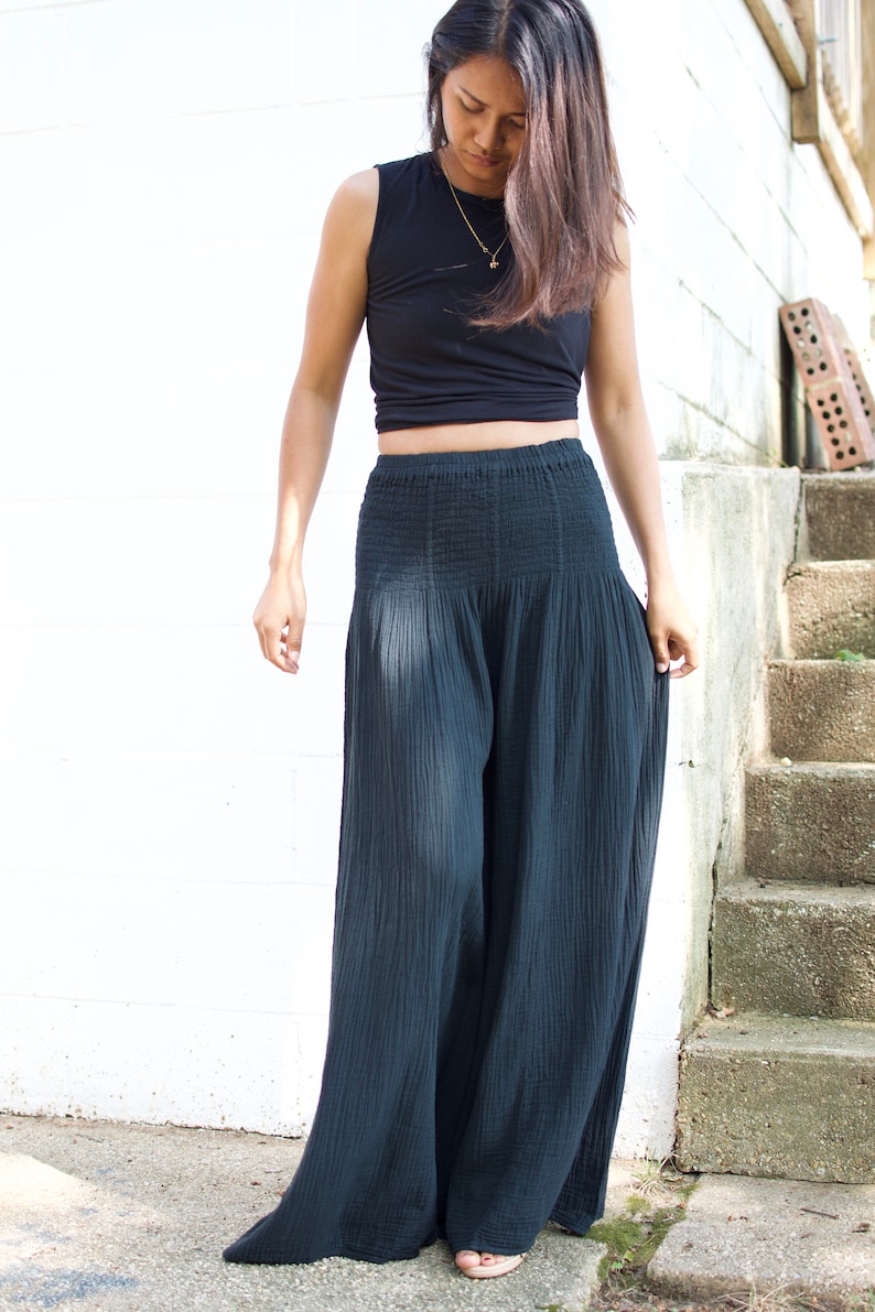 May include: A woman wearing a black crop top and wide-legged black pants. The pants have a smocked waistband and are made of a lightweight fabric.