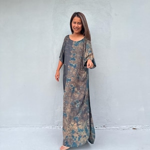 Może przedstawiać: Długa, zwiewna sukienka z wzorem tie-dye w odcieniach niebieskiego, brązowego i beżowego. Sukienka ma luźny, wygodny kr&oacute;j i okrągły dekolt.