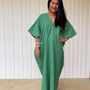 May include: A green caftan dress with a V-neck and wide sleeves. The dress is made of a lightweight fabric and has a relaxed fit. The text "MALA handworks Hollywood, MD" is visible.