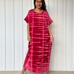 May include: A long, red tie-dye maxi dress with short sleeves. The dress has a relaxed fit and a round neckline.