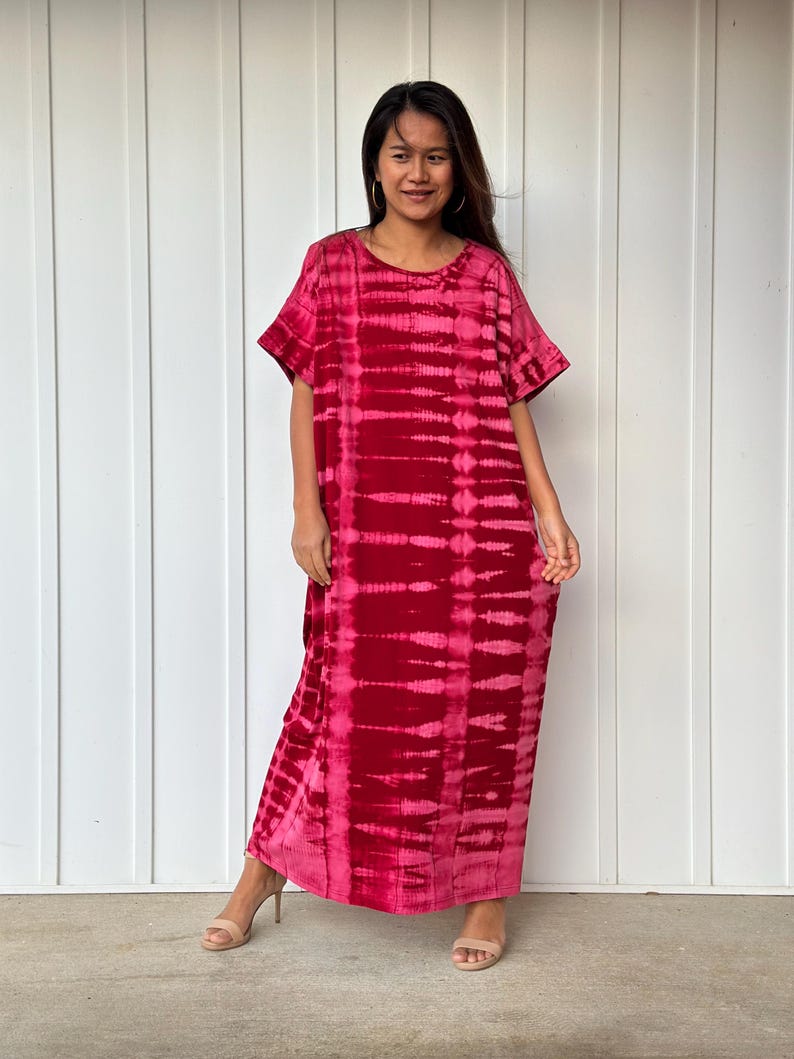 May include: A long, red tie-dye maxi dress with short sleeves. The dress has a relaxed fit and a round neckline.