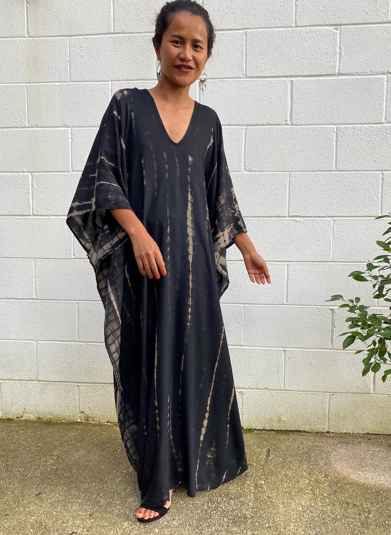 May include: A black and beige tie-dye kaftan with a V-neckline and long sleeves. The kaftan is made of a soft, flowing fabric and has a relaxed fit.