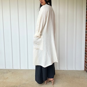 Pu&ograve; includere: Un cardigan bianco a maniche lunghe, leggero e aperto sul davanti, con tasche. Il cardigan &egrave; realizzato in un tessuto morbido e testurizzato e viene indossato sopra una gonna maxi nera.
