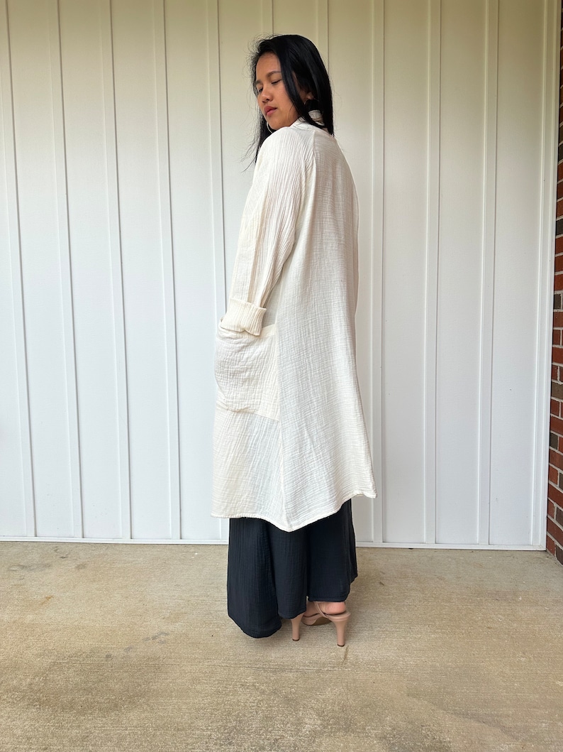 Pu&ograve; includere: Un cardigan bianco a maniche lunghe, leggero e aperto sul davanti, con tasche. Il cardigan &egrave; realizzato in un tessuto morbido e testurizzato e viene indossato sopra una gonna maxi nera.