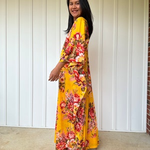 May include: A yellow maxi dress with a floral print. The dress has a V-neckline and 3/4 sleeves. The dress is flowy and has a relaxed fit.