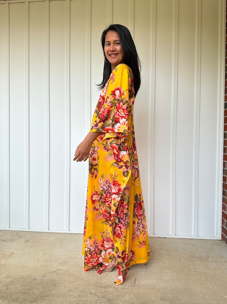 May include: A yellow maxi dress with a floral print. The dress has a V-neckline and 3/4 sleeves. The dress is flowy and has a relaxed fit.