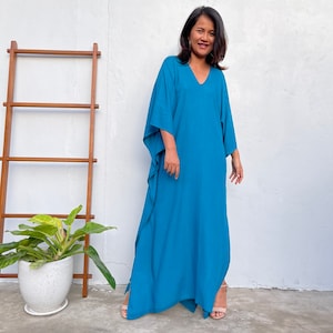May include: A woman wearing a long, flowing teal blue maxi dress with a V-neckline. The dress has a relaxed fit and is made of a lightweight fabric.