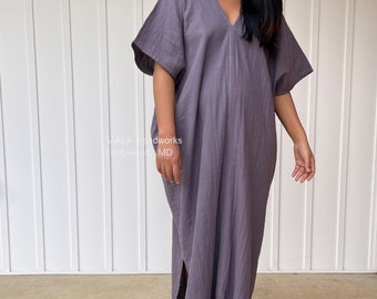 May include: A long, flowing, gray dress with a V-neck and short sleeves. The dress has a slit on the side and is made of a soft, textured fabric. The text "MALA handworks Hollywood, MD" is visible.