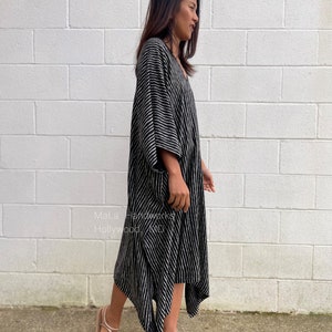 K&ouml;nnte beinhalten: Ein schwarz-wei&szlig; gestreiftes Maxikleid mit V-Ausschnitt und flie&szlig;ender Silhouette. Das Kleid hat eine lockere Passform und ist perfekt f&uuml;r einen l&auml;ssigen Sommerlook. Das Model tr&auml;gt das Kleid mit Sandalen.