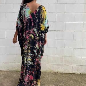 May include: A long, black maxi dress with a tie-dye pattern in shades of pink, yellow, and blue. The dress has a V-neck and short sleeves.