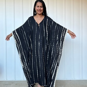 May include: A black and white striped kaftan with a tie closure at the neckline. The kaftan is made of a soft, flowing fabric and has a relaxed fit.