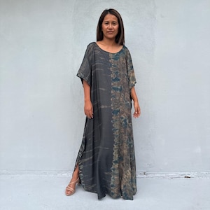 Może przedstawiać: Długa, zwiewna sukienka maxi z wzorem tie-dye w odcieniach brązu, zieleni i czerni. Sukienka ma luźny, wygodny kr&oacute;j i rozcięcie z boku.