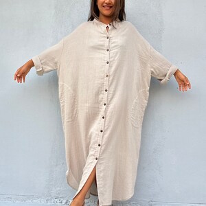 May include: A long, beige, button-down shirt dress with a relaxed fit and a front slit. The dress has a collar and long sleeves.