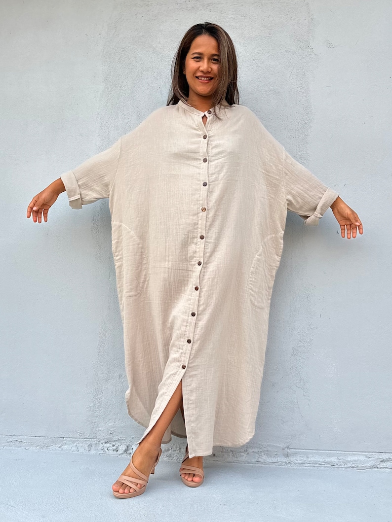 May include: A long, beige, button-down shirt dress with a relaxed fit and a front slit. The dress has a collar and long sleeves.