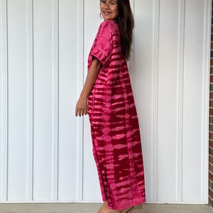 May include: A long, pink tie-dye dress with a short sleeve and a v-neck. The dress is made of a soft, flowing fabric and has a relaxed fit.