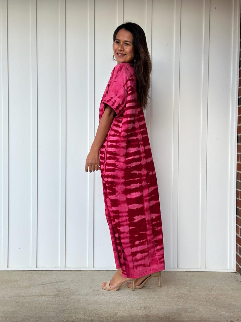 May include: A long, pink tie-dye dress with a short sleeve and a v-neck. The dress is made of a soft, flowing fabric and has a relaxed fit.