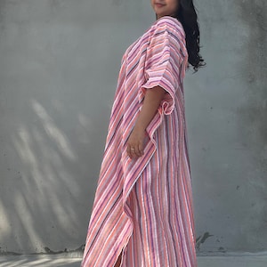 May include: A woman wearing a long, pink and white striped dress with a flowing silhouette. The dress has a V-neckline and a relaxed fit.
