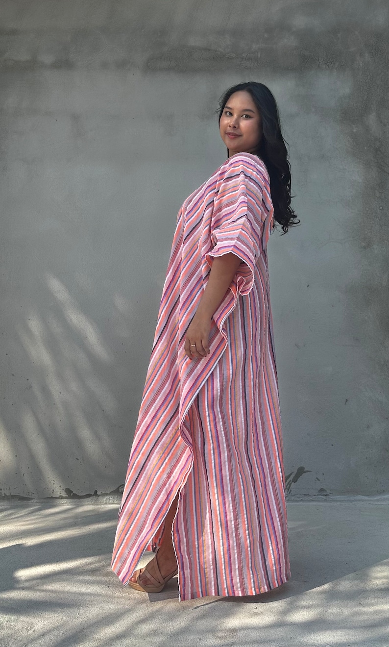 May include: A woman wearing a long, pink and white striped dress with a flowing silhouette. The dress has a V-neckline and a relaxed fit.