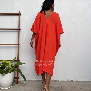 May include: A bright orange, loose-fitting, knee-length dress with a V-neck and short sleeves. The dress is made of a soft, textured fabric. The text "MALA handworks Hollywood, MD" is printed on the dress.