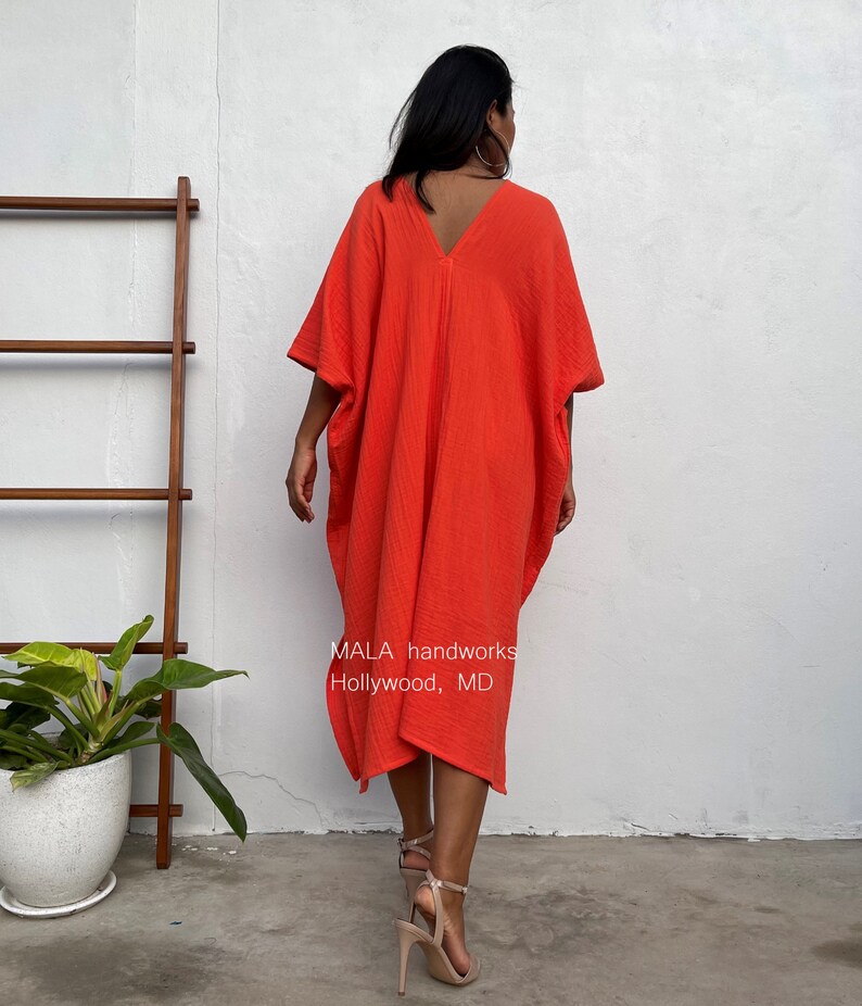 May include: A bright orange, loose-fitting, knee-length dress with a V-neck and short sleeves. The dress is made of a soft, textured fabric. The text "MALA handworks Hollywood, MD" is printed on the dress.