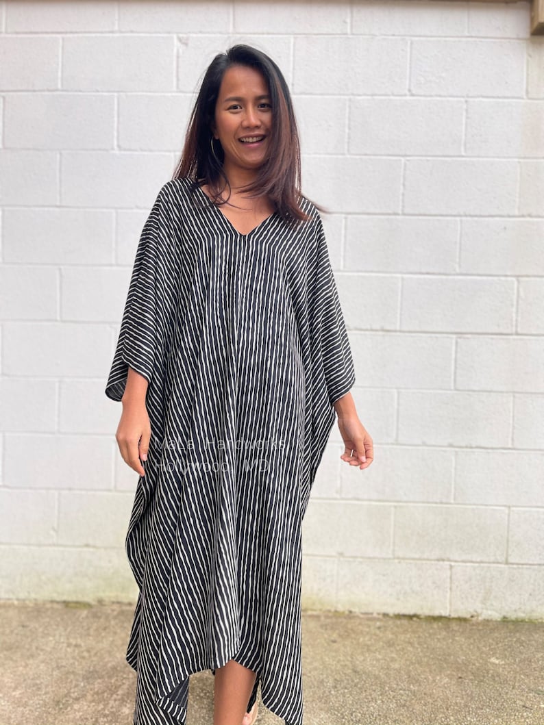 K&ouml;nnte beinhalten: Ein schwarz-wei&szlig; gestreiftes Maxikleid mit V-Ausschnitt. Das Kleid hat eine flie&szlig;ende, lockere Passform und ist aus einem leichten Stoff gefertigt.