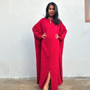 May include: A long, red, button-down dress with a slit in the front. The dress is made of a soft, textured fabric.