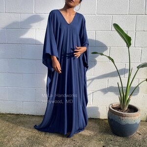 May include: A navy blue maxi dress with a V-neck and long sleeves. The dress is made of a soft, flowing fabric and has a relaxed fit. The dress is shown being worn by a person standing in front of a white brick wall. The text "MaLa Handworks Hollywood, MD" is visible on the dress.
