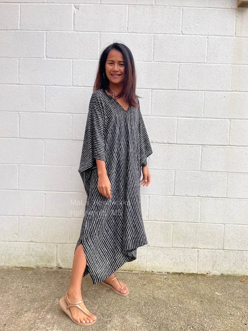 K&ouml;nnte beinhalten: Ein schwarz-wei&szlig; gestreiftes Maxikleid mit V-Ausschnitt und langen &Auml;rmeln. Das Kleid hat eine lockere Passform und eine flie&szlig;ende Silhouette. Das Model tr&auml;gt das Kleid mit Sandalen.