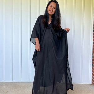 May include: A black maxi dress with a V-neckline and long sleeves. The dress has a flowing silhouette and a relaxed fit.