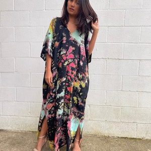 May include: A long, black maxi dress with a tie-dye pattern in shades of pink, blue, and yellow. The dress has a V-neck and short sleeves. It features side slits and is made of a soft, flowing fabric.