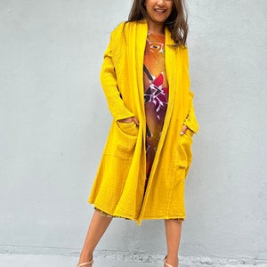 May include: A long, yellow cardigan with a shawl collar and pockets. The cardigan is made of a soft, textured fabric.