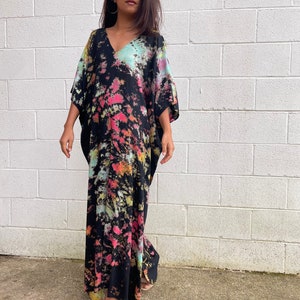 May include: A long, black maxi dress with a tie-dye pattern in shades of pink, blue, and yellow. The dress has a V-neck and short sleeves.