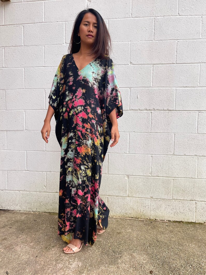 May include: A long, black maxi dress with a tie-dye pattern in shades of pink, blue, and yellow. The dress has a V-neck and short sleeves.