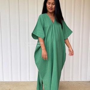 May include: A long, flowing green dress with a V-neck and wide sleeves. The dress is made of a soft, lightweight fabric and has a relaxed fit. The text "MALA handworks Hollywood MD" is visible on the left side of the image.