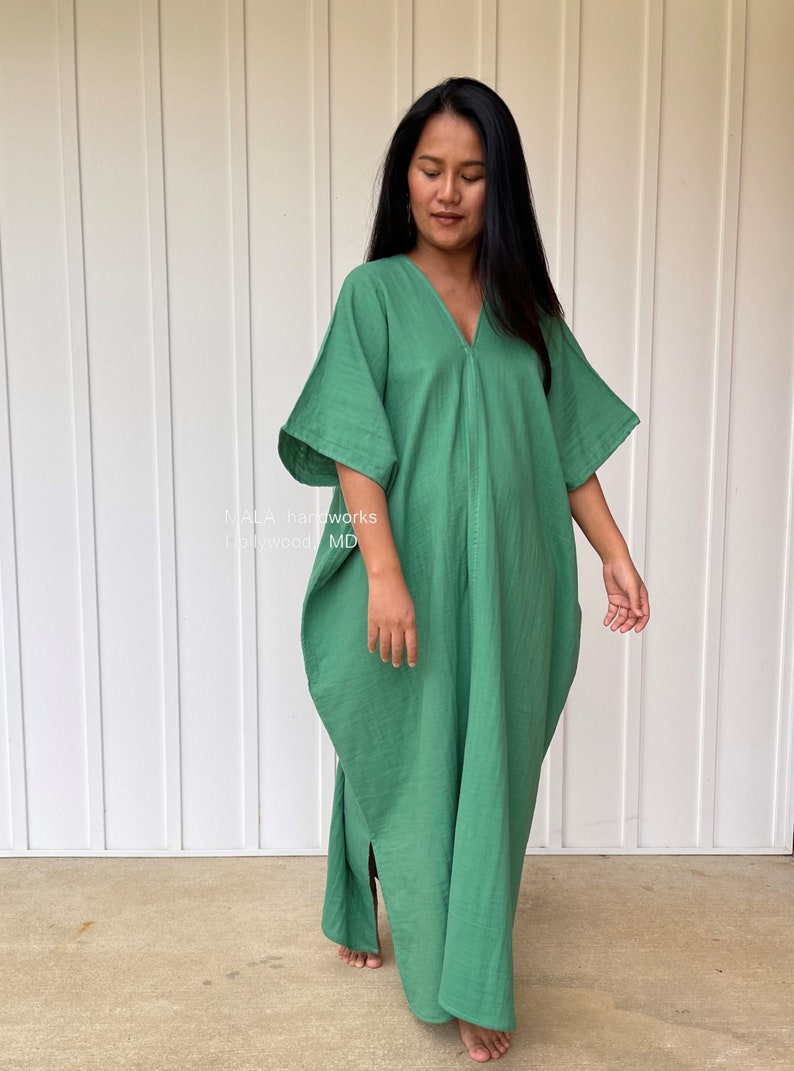 May include: A long, flowing green dress with a V-neck and wide sleeves. The dress is made of a soft, lightweight fabric and has a relaxed fit. The text "MALA handworks Hollywood MD" is visible on the left side of the image.