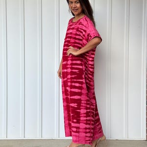 May include: A long, pink and white tie-dye maxi dress with short sleeves. The dress has a relaxed fit and is made of a soft, comfortable fabric.