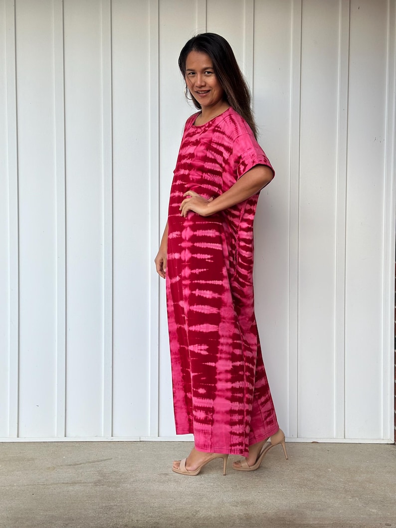 May include: A long, pink and white tie-dye maxi dress with short sleeves. The dress has a relaxed fit and is made of a soft, comfortable fabric.