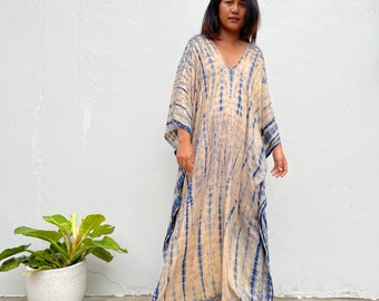 May include: A long, flowing, beige maxi dress with a blue tie-dye pattern. The dress has a V-neck and 3/4 sleeves.