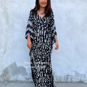 May include: A black and white kaftan with a leopard print design. The kaftan has a V-neck and long sleeves. The model is wearing the kaftan with a pair of sandals.