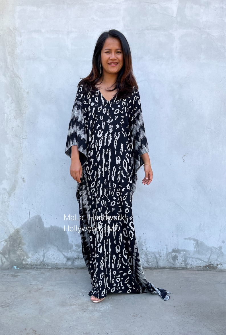 May include: A black and white kaftan with a leopard print design. The kaftan has a V-neck and long sleeves. The model is wearing the kaftan with a pair of sandals.
