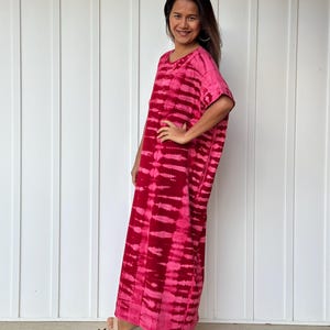 May include: A long, pink and white tie-dye maxi dress with short sleeves. The dress is loose fitting and has a relaxed silhouette.