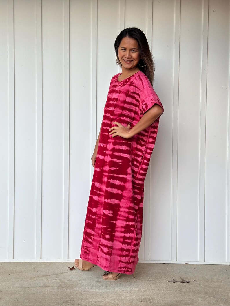 May include: A long, pink and white tie-dye maxi dress with short sleeves. The dress is loose fitting and has a relaxed silhouette.