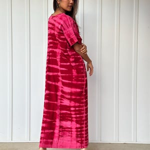 May include: A long, pink and red tie-dye maxi dress with short sleeves. The dress is made of a soft, flowing fabric and has a relaxed fit.