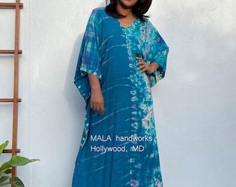 May include: A long, flowing blue and purple tie-dye kaftan with a V-neckline. The kaftan is made of a soft, lightweight fabric and has a relaxed fit. The text "MALA handworks Hollywood, MD" is printed on the front of the kaftan.