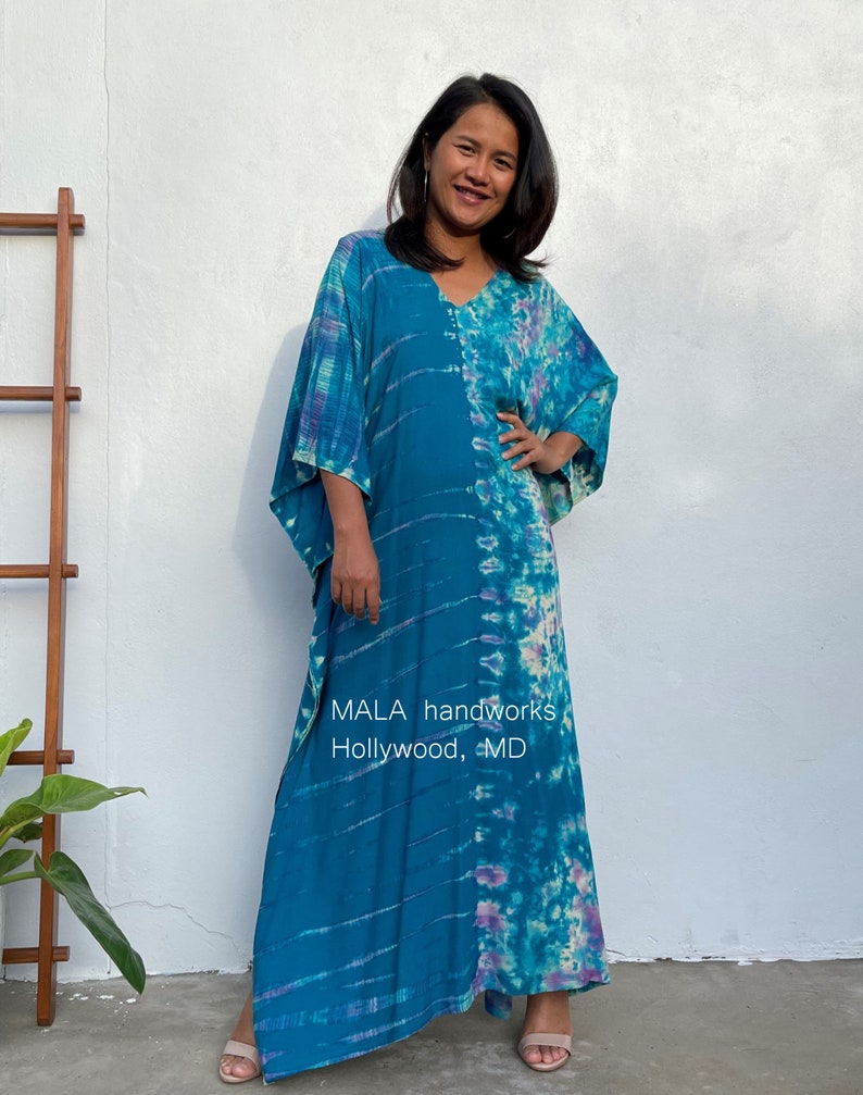May include: A long, flowing blue and purple tie-dye kaftan with a V-neckline. The kaftan is made of a soft, lightweight fabric and has a relaxed fit. The text "MALA handworks Hollywood, MD" is printed on the front of the kaftan.
