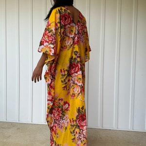 May include: A yellow maxi dress with a floral print featuring red, pink, and white flowers. The dress has a V-neckline and a flowing silhouette.