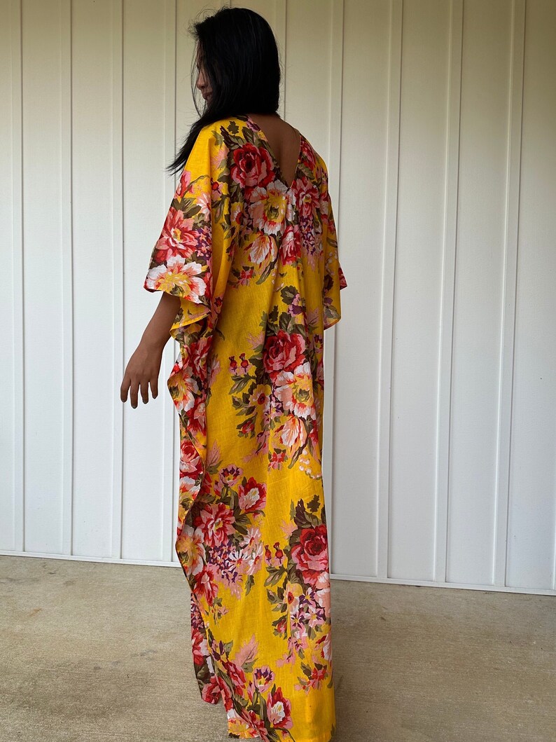 May include: A yellow maxi dress with a floral print featuring red, pink, and white flowers. The dress has a V-neckline and a flowing silhouette.